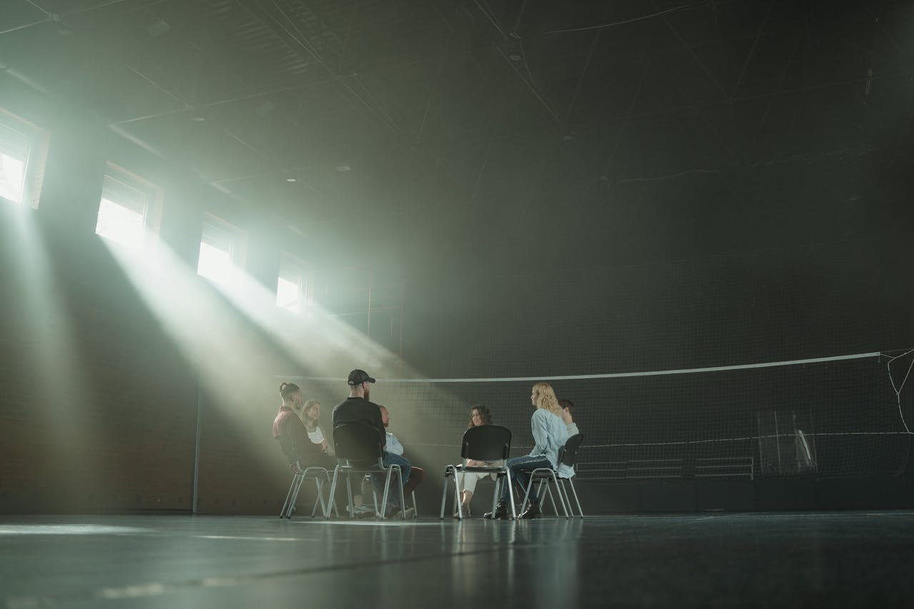 team-03 A small group of people participating in a support session, illuminated by sunrays in a spacious hall.